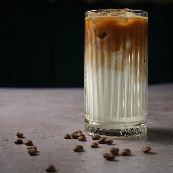 Iced coffee with milk in a tall ribbed glass, surrounded by scattered coffee beans.