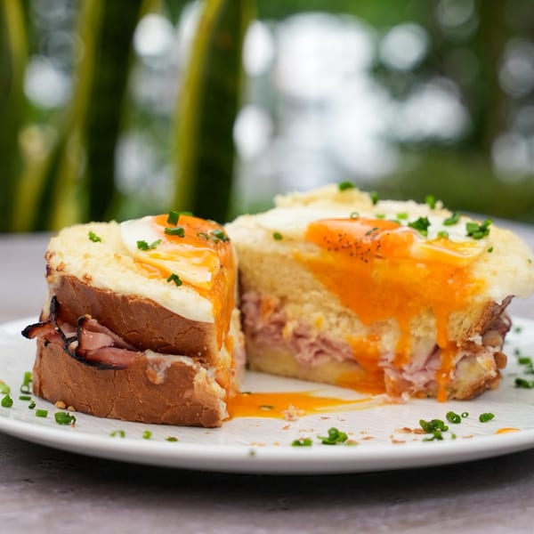 Two halves of a croque madame sandwich with runny egg yolks and chives on a white plate.