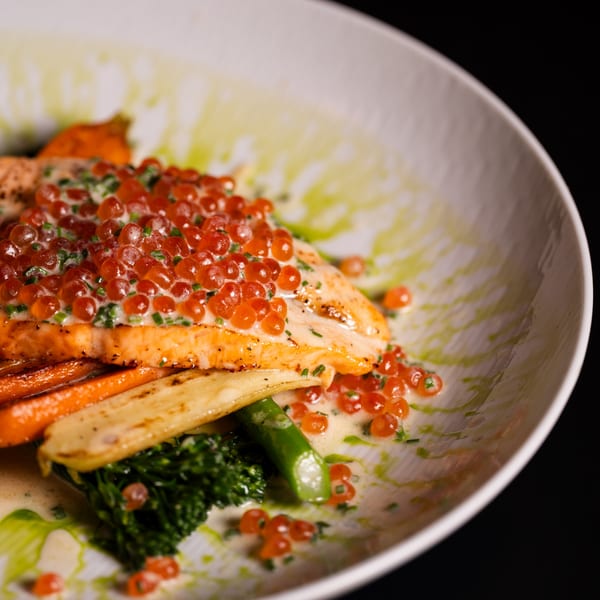 Pan-seared salmon topped with red caviar and chives, served with roasted vegetables and a creamy sauce.