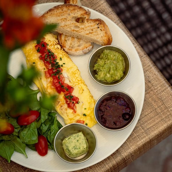 Savory omelet topped with diced tomatoes and herbs, served with toasted bread, guacamole, beans, seasoned butter, and salad.