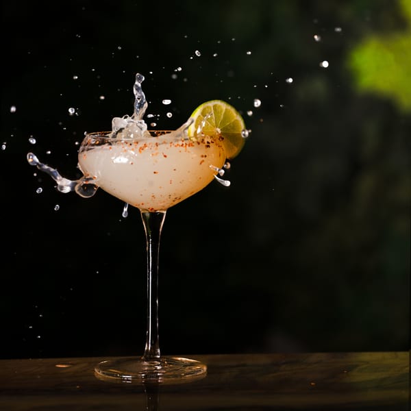 A cocktail in a martini glass with a lime wedge, splashing liquid against a dark background.