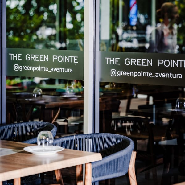 Restaurant exterior with "THE GREEN POINTE" sign on glass, showing indoor dining tables and chairs.