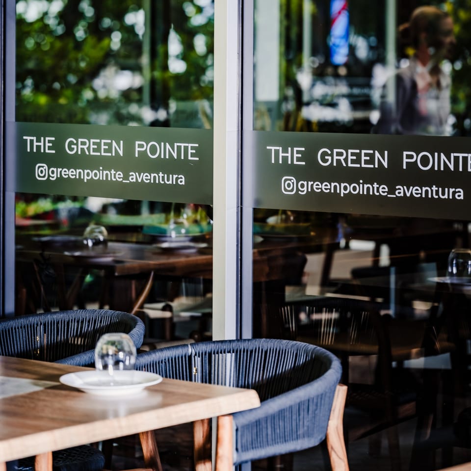 Restaurant exterior with "THE GREEN POINTE" sign on glass, showing indoor dining tables and chairs.