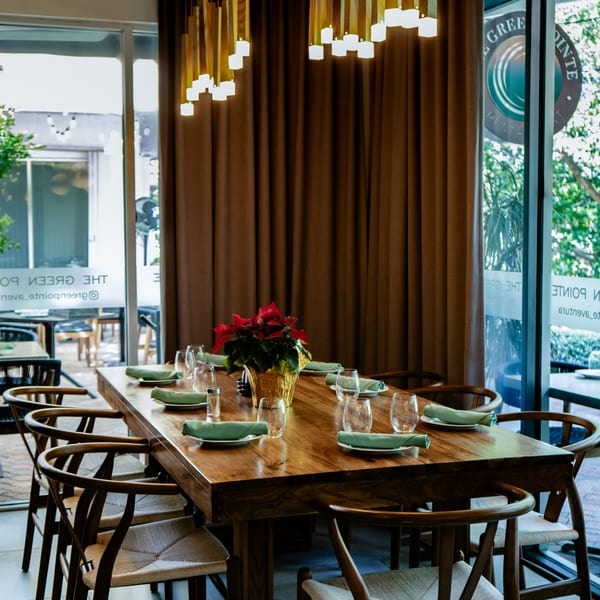 A long wooden dining table set with green napkins and glasses, featuring a poinsettia centerpiece.