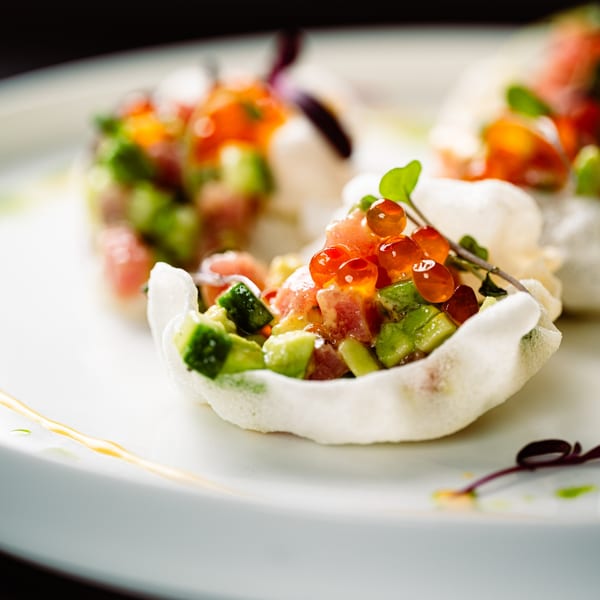 Close-up of three shrimp chips filled with diced tuna, avocado, and bright orange roe.