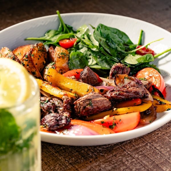 Grilled steak and vegetables with roasted potatoes and a side salad, next to a drink.