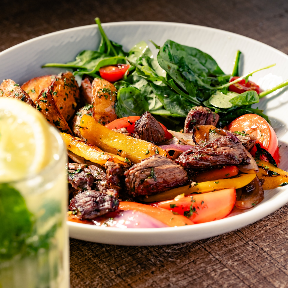 Grilled steak and vegetables with roasted potatoes and a side salad, next to a drink.